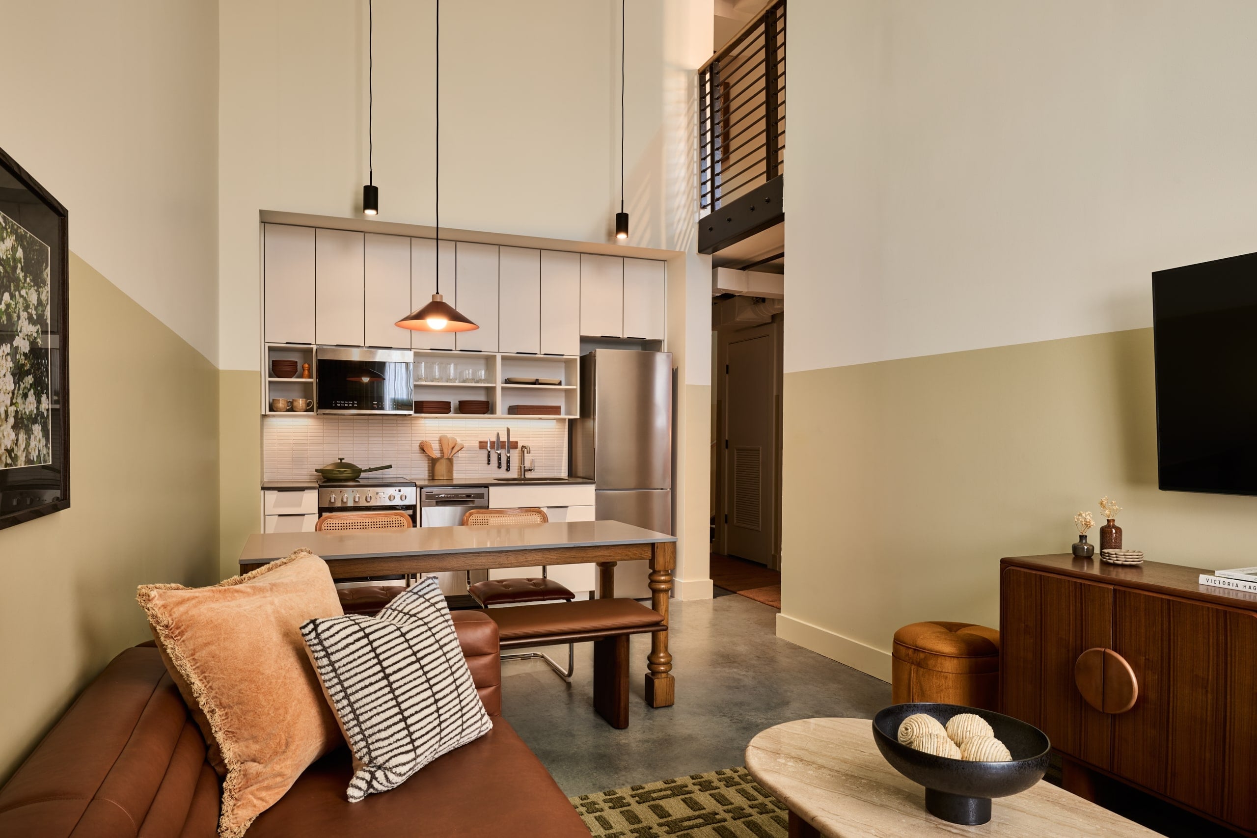 Modern loft suite with open kitchen, dining table, leather seating, and staircase to upper level