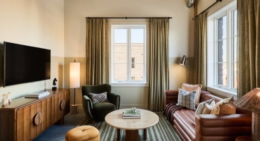 Elegant hotel suite living room with brown leather sofa, wooden media console, and large windows