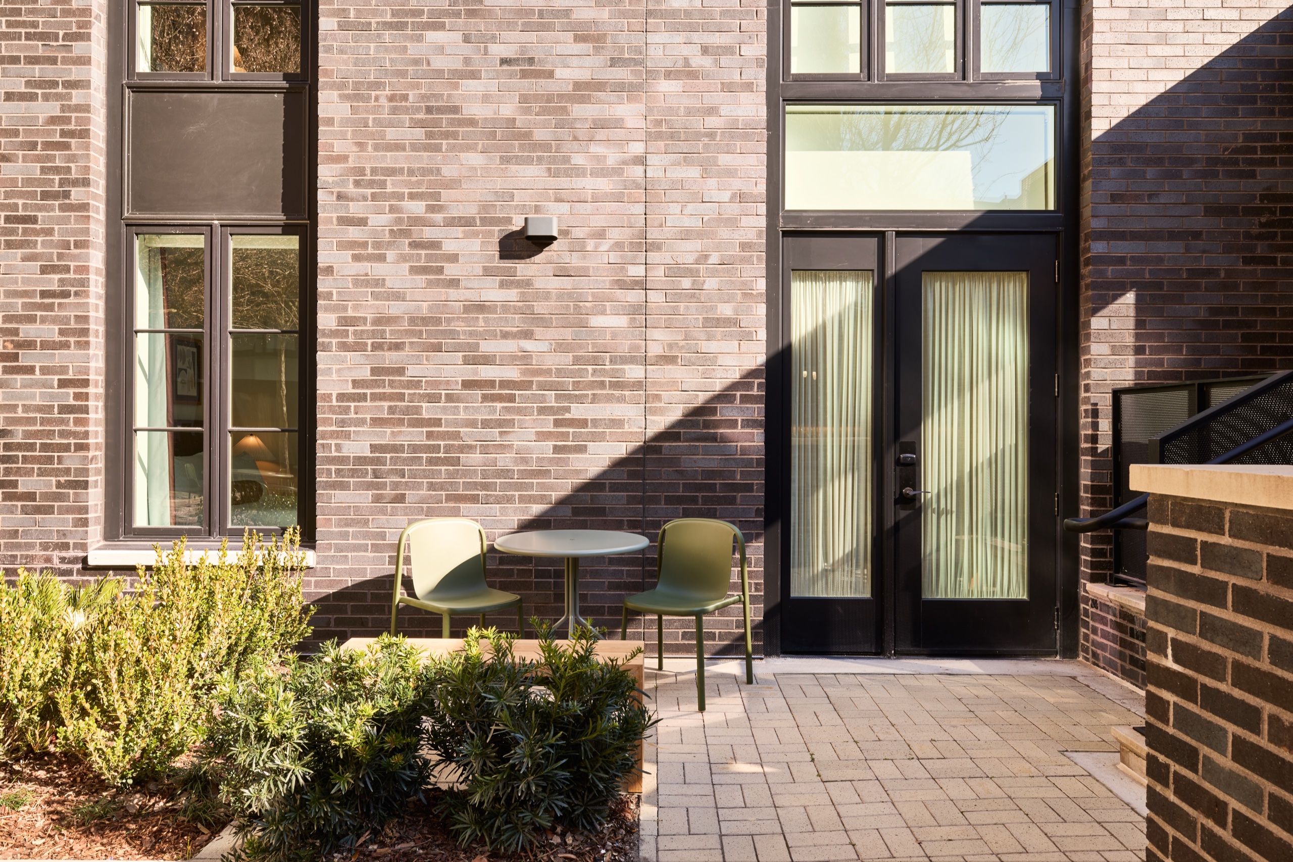 Private brick patio with bistro table and green chairs outside a suite's glass doors at The Ann Savannah