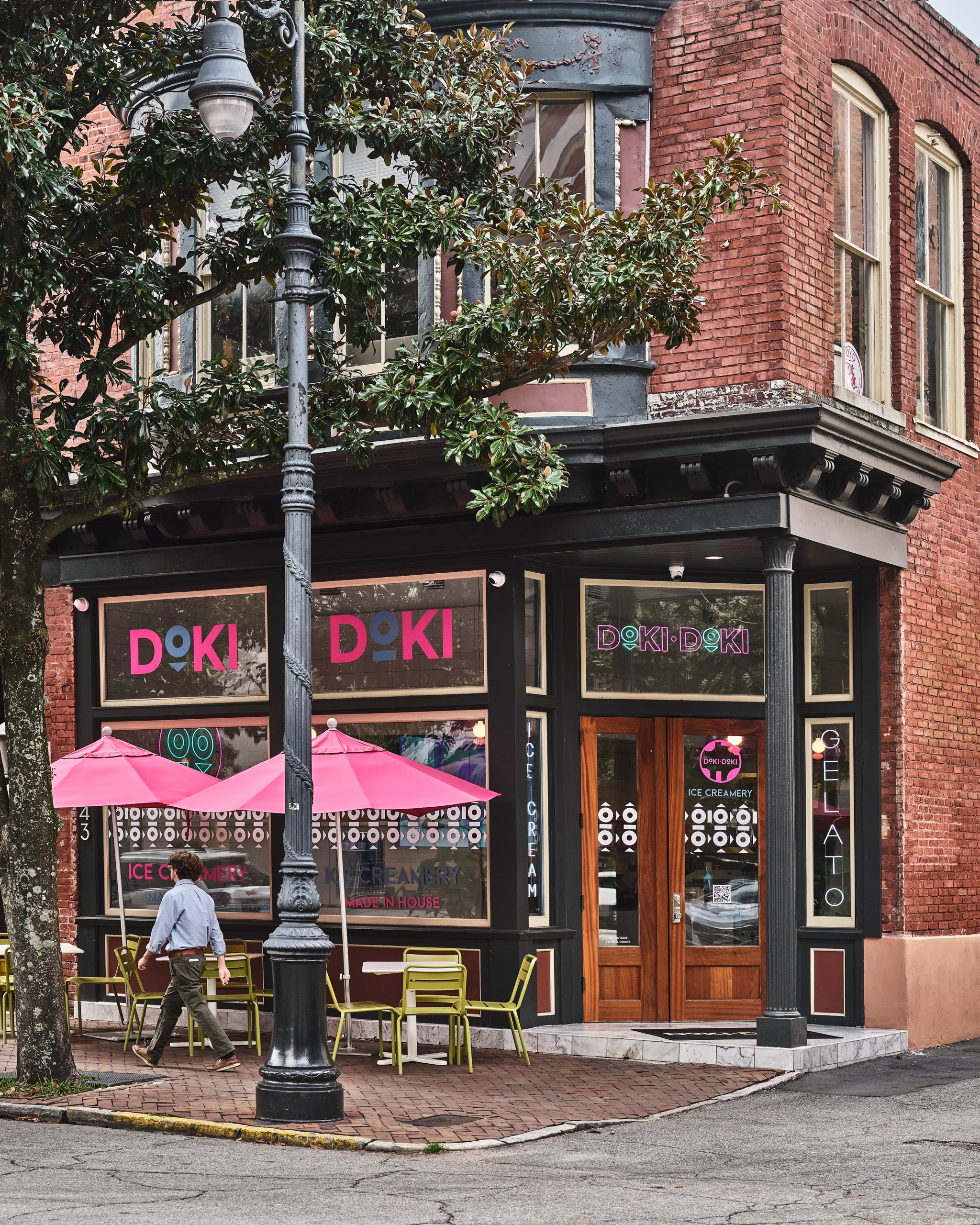 Doki Doki Ice Creamery on a historic brick corner building with pink umbrellas and green bistro chairs outside.
