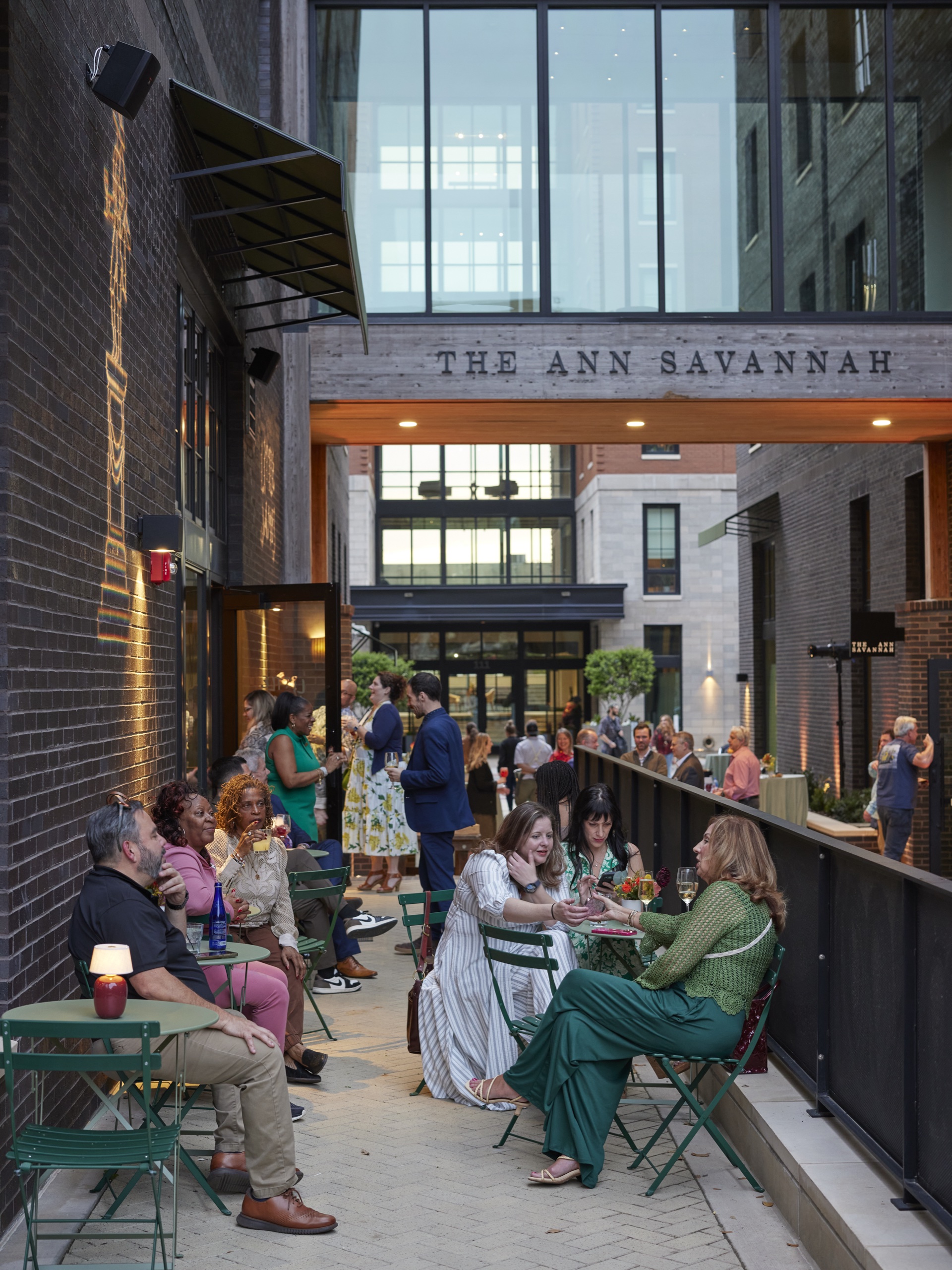 Guests socializing at outdoor bistro tables during The Ann Savannah hotel grand opening event at dusk.
