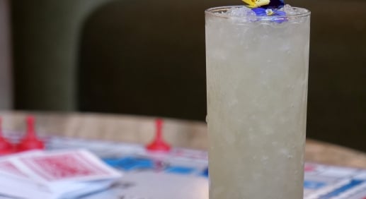 Tall frosted glass filled with crushed ice and a yellow-purple flower garnish on a colorful game-board surface (Monopoly-like).