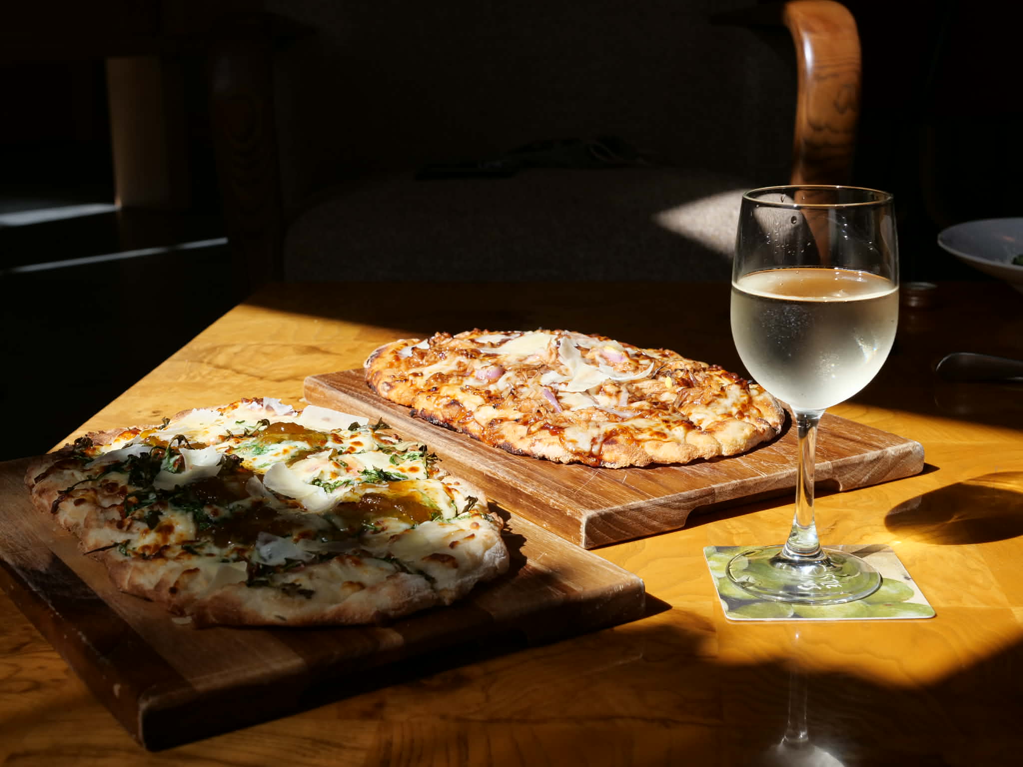 Two artisan flatbread pizzas on rustic wooden boards with a glass of white wine at Little James