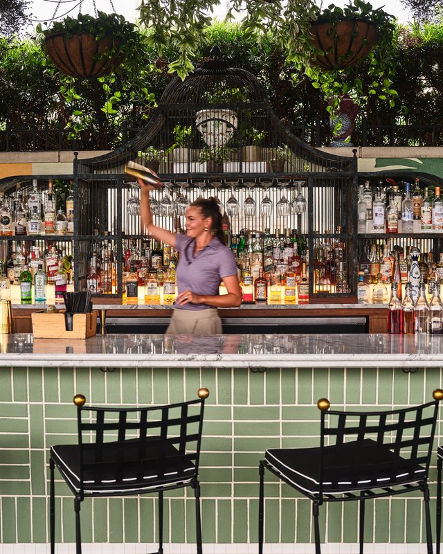 Bartender tossing a cocktail shaker at the outdoor bar with a sage-green tile front
